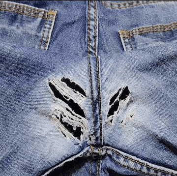 Um par de jeans sendo reparado manualmente com técnicas de costura para corrigir um buraco, usando agulha, linha e tecido semelhante ao jeans original.