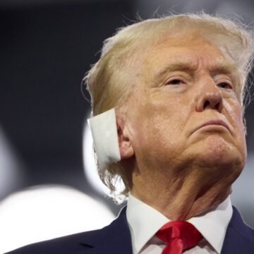 Imagem de Donald Trump, vestido formalmente, discursando em um comício enquanto gesticula energicamente, representando sua postura política assertiva.