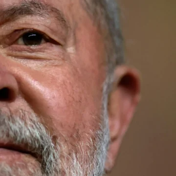Lula discursando em um palanque iluminado, cercado por apoiadores segurando bandeiras, com uma expressão séria que reflete o peso de sua trajetória política. Ao fundo, um céu de final de tarde, simbolizando uma transição ou encerramento de ciclo.