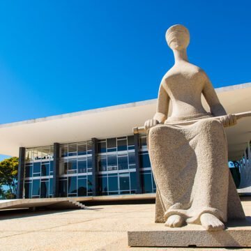 Fachada do Supremo Tribunal Federal (STF), com a estátua da Justiça em primeiro plano, em um dia ensolarado.