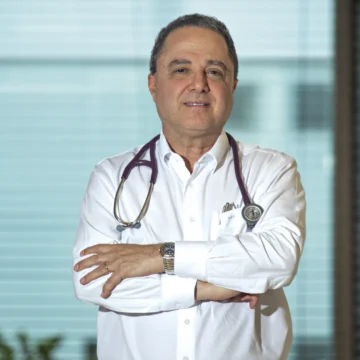 Imagem do presidente Lula sorrindo, sentado em uma cadeira em ambiente interno, ao lado de um médico.
