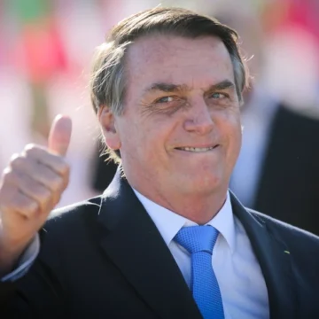 Jair Bolsonaro gesticulando durante entrevista, com expressão firme, ao fundo um cenário político sugerindo disputa.