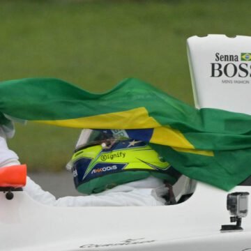 Ayrton Senna em sua icônica McLaren, com capacete amarelo e expressão de concentração, cruzando uma curva em alta velocidade durante uma corrida de Fórmula 1.