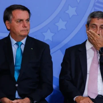 Jair Bolsonaro e Braga Netto participando de um evento oficial, ambos de terno, com expressões de seriedade, capturados em um momento de diálogo político intenso.