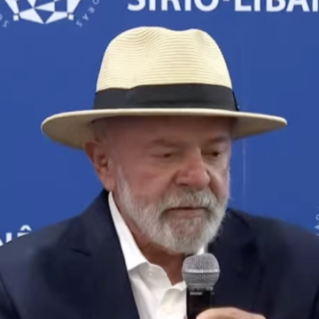 Presidente Lula acena para jornalistas ao sair do Hospital Sírio-Libanês, com uma equipe médica ao fundo