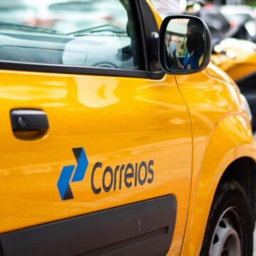 Fachada de uma agência dos Correios com placa visível, destacando o logotipo da estatal em amarelo e azul.
