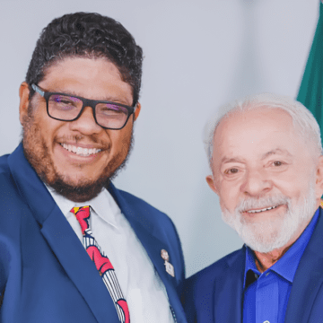 Imagem de Alexandre Brasil Fonseca ao lado do presidente Lula, em um evento público, mostrando um sorriso e proximidade.