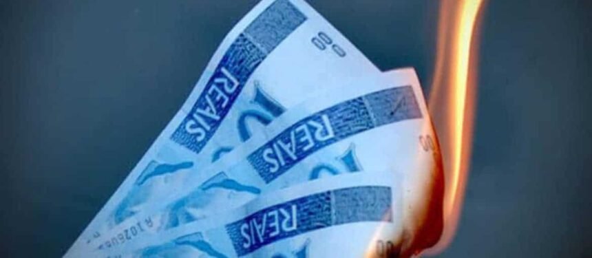 Cédulas de dólar espalhadas sobre uma mesa de madeira, ao lado de gráficos financeiros digitais mostrando flutuações da moeda americana.