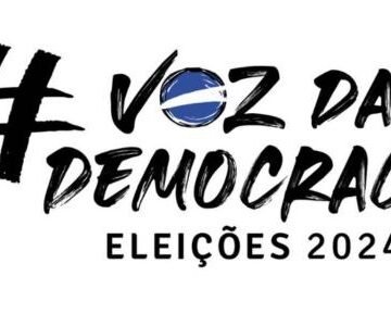 Multidão de pessoas votando em uma urna eletrônica, com foco em uma mão inserindo o voto.