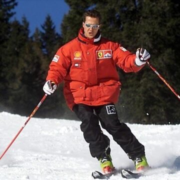 Imagem de Michael Schumacher comemorando um título na Fórmula 1, com um capacete vermelho e o pódio ao fundo.