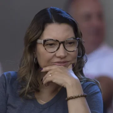A primeira-dama Janja, sorrindo e usando óculos de sol, participa de um evento público ao lado do presidente Lula.