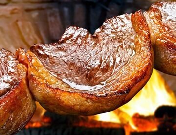 Picanha suculenta sendo preparada em uma churrasqueira, com faíscas e fumaça ao redor, transmitindo a sensação de um churrasco delicioso e caro.
