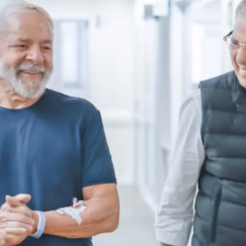 Lula caminhando em um corredor de hospital, acompanhado de médicos e sorrindo, com curativos visíveis na cabeça.
