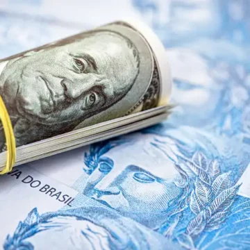 Cédulas de dólar americano empilhadas, simbolizando a alta da moeda.