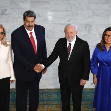 Imagem de uma bandeira do Brasil e da Venezuela se sobrepondo em um fundo de cores neutras.
