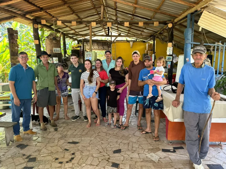 Uma imagem horizontal que mostra os membros da família Bettim em meio à plantação de café, em sua fazenda. Eles estão em grupos, com alguns olhando para a câmera e outros trabalhando. A cena transmite a conexão da família com a terra e a dedicação ao trabalho.