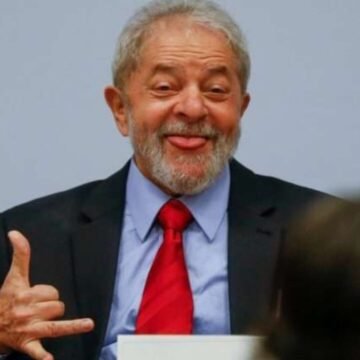 Lula sorrindo em um evento, segurando um papel com o logo do governo.